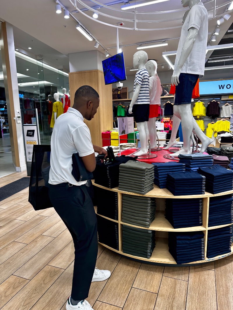 A UNIQ shop assistant sweeping an RFID scanner across stacked t-shirts